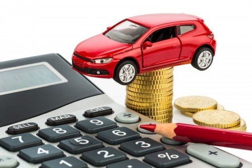 Red toy car on stack of coins next to a calculator for estimating car loan payments