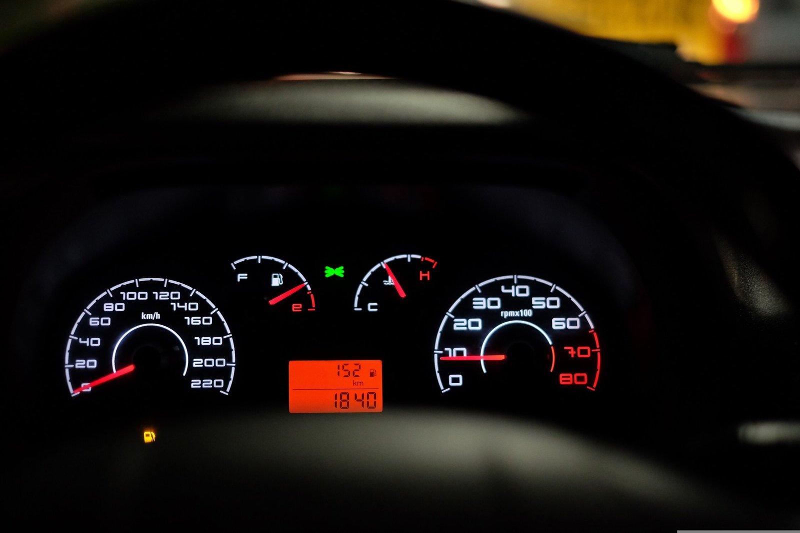 Car dashboard at night showing the fuel gauge near empty with the low fuel warning light on