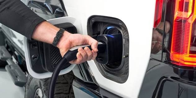 Person plugging a charging cable into the charge port of a white electric pickup truck