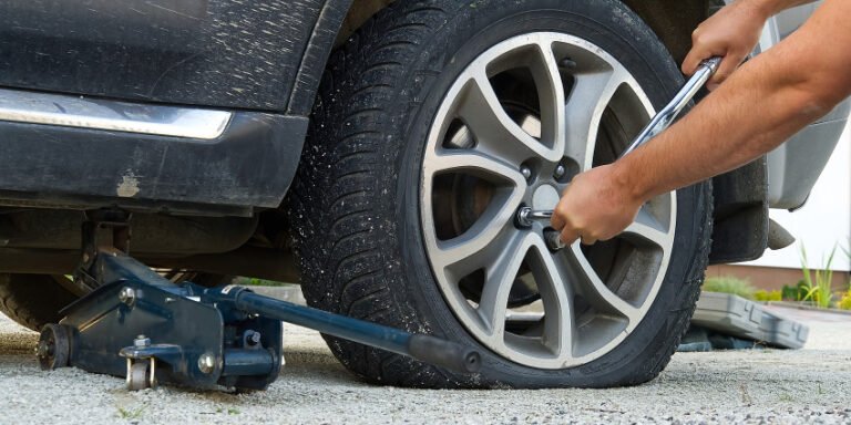 Man using a lug wrench to loosen the wheel while changing a flat tire with a jack