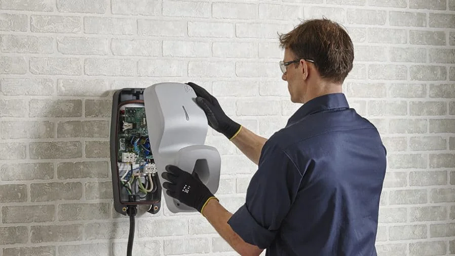 Electrician fitting the cover onto a wall-mounted EV charger with internal wiring visible