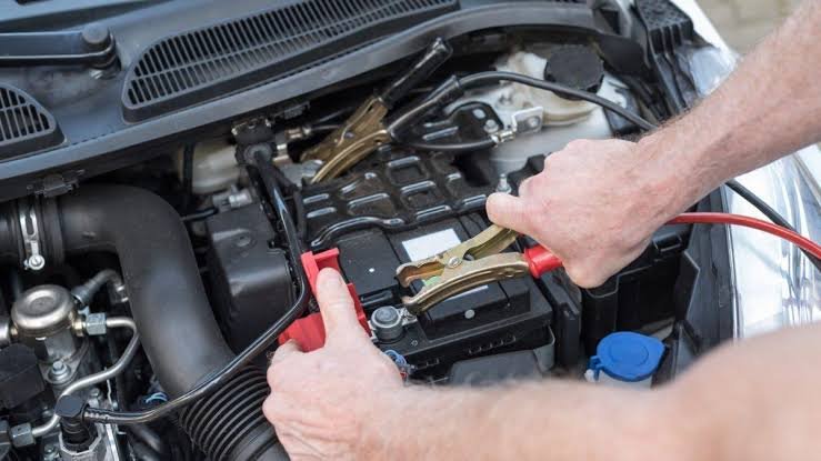 Mechanic attaching red jumper cable clamp to a car battery terminal